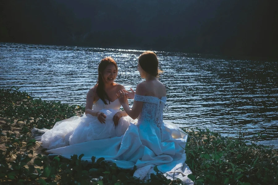 Two brides sitting on the shore of a lake