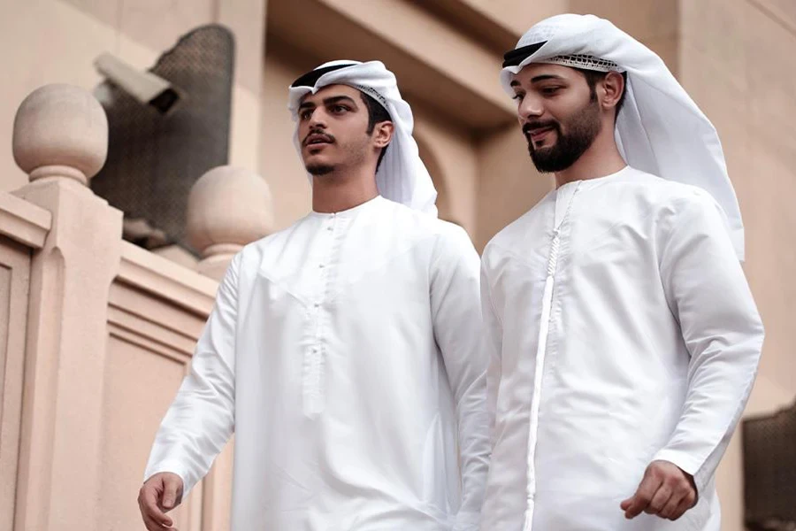 Two men in white dishdashas while walking