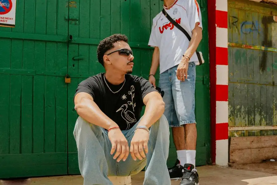 Two men sitting on the ground in front of a green and red building by Ayoub Moukhliss