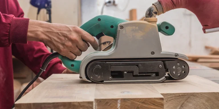 Using a hand-held sanding machine or belt sander to level the surface of a glued wood for a cabinet