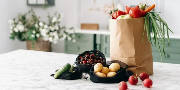 Verschiedene Gemüsesorten in Einkaufstüten aus Papier und schwarzen Netzbeuteln auf Kücheninsel