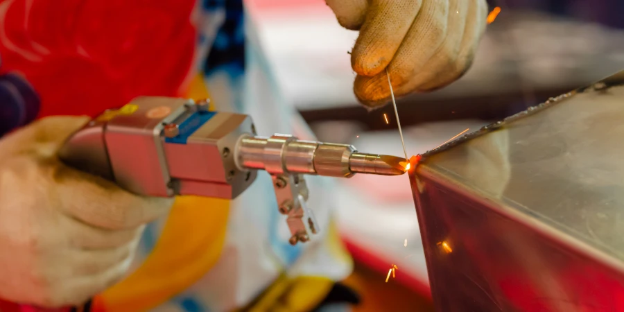 Welder hands using portable handheld laser welding machine with sparks - close up