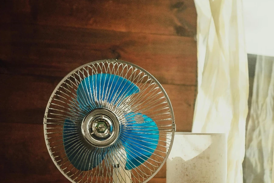 White and Blue Desk Fan beside Wooden Wall