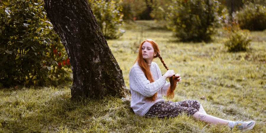 Woman Sitting on Green Grass Braiding Hair