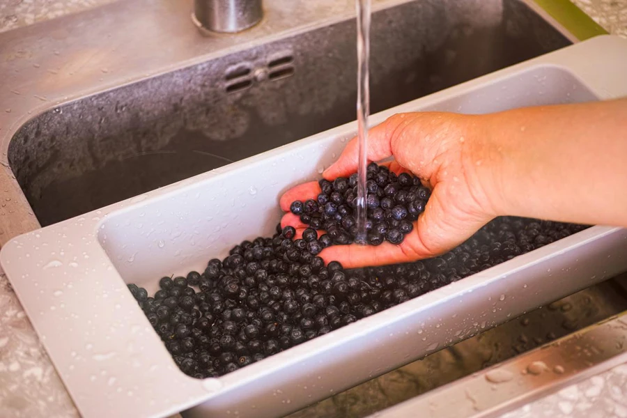 Woman hand washing blueberries in kitchen sink. Close-up.