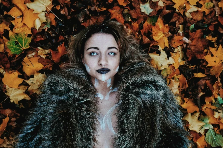 Woman in Black Fur Coat Laying on Brown Maple Leaves