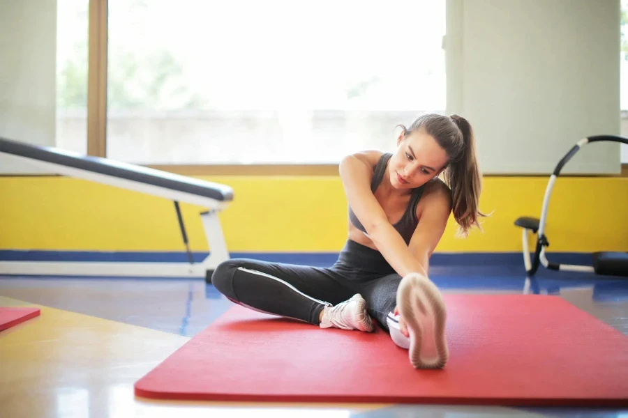 Woman in Black Sports Bra and Black Legging Sitting on Red Yoga Mat