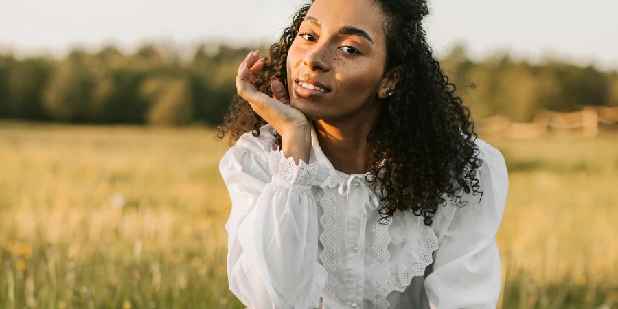 Woman in White Long Sleeve Blouse and Brown Skirt Sitting on Green Grass Field