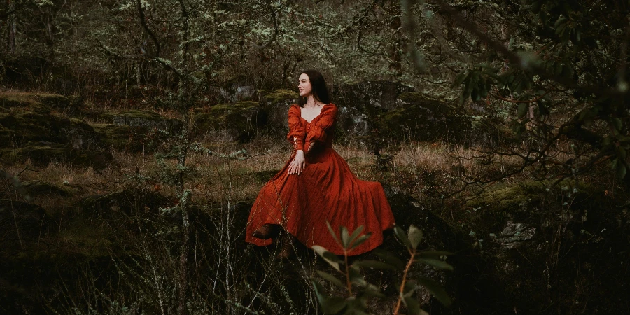 Mujer con un vestido medieval rojo sentada en una roca en el bosque