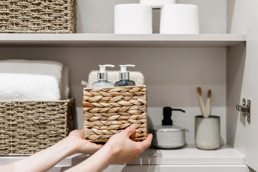 Woman put wicker box with cosmetics products in bathroom closet