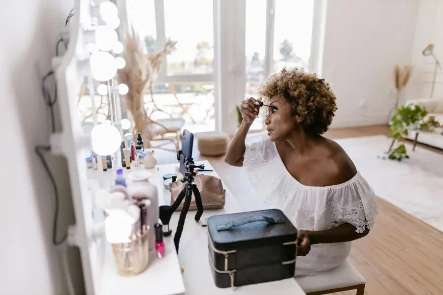 Woman with Afro Hairstyle Applying Mascara in Front of a Mirror by RDNE Stock project