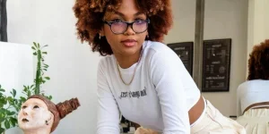 Femme aux cheveux bouclés rouges dans des lunettes assise dos au miroir