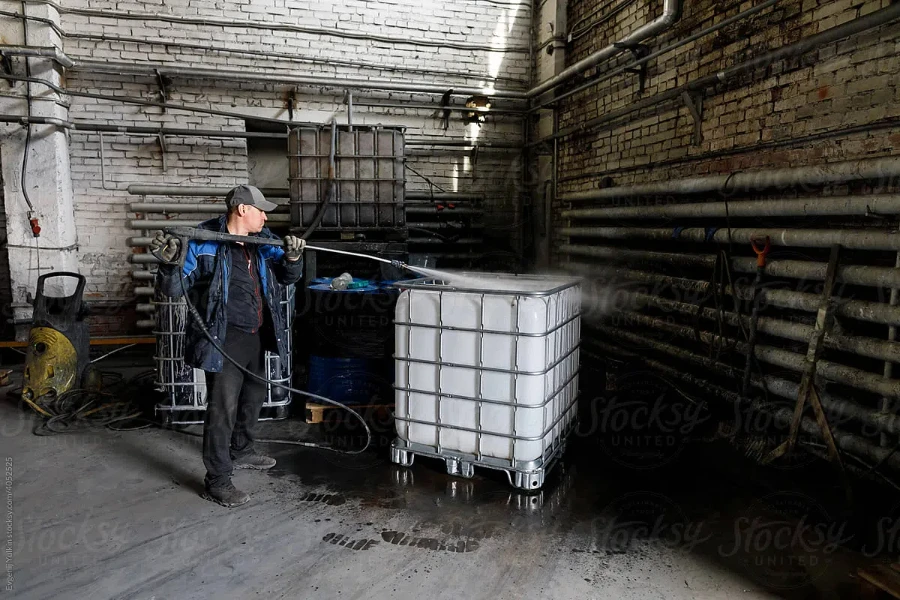 Worker cleans plactic container using high pressure washer