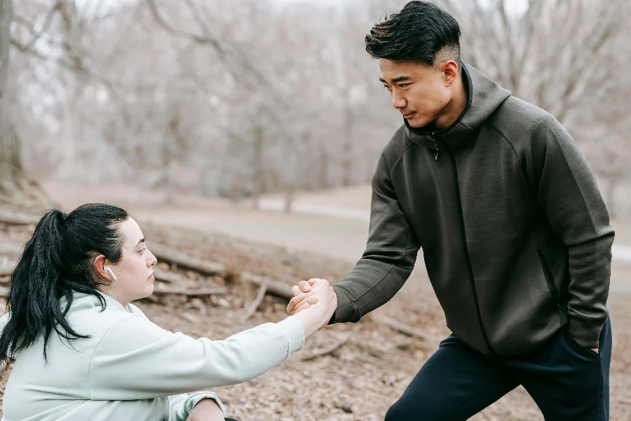 Young Asian male in sportswear giving hand to plump female fell on ground