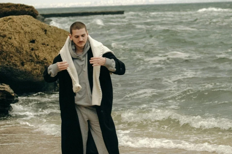 Young Short-hair Man in Sportswear Wearing Long Warm Coat and Posing at Seashore