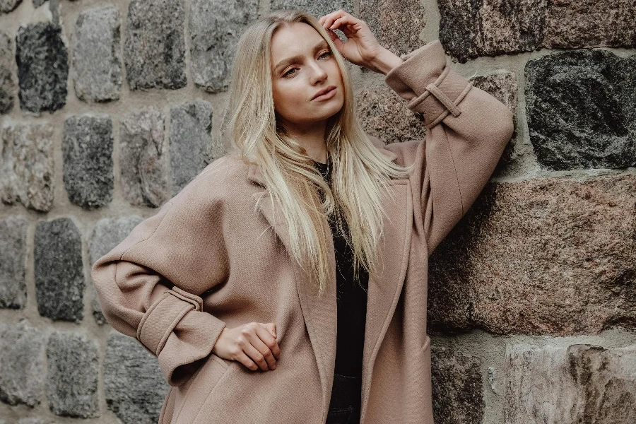 Young Woman in a Wool Winter Coat Leaning against a Building Facade