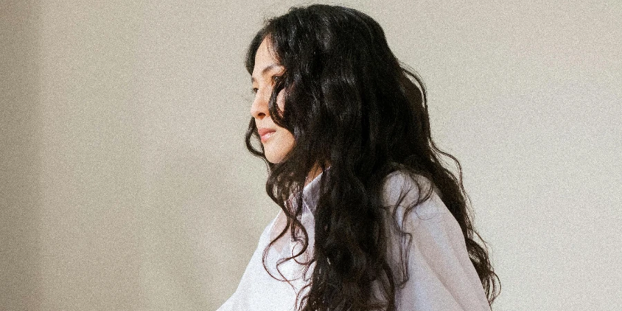 Young Woman with Black Curly Hair Sitting in Bed in White Pyjamas