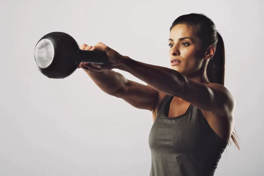 Young fitness female exercise with kettle bell. Mixed race woman doing gym workout on grey background