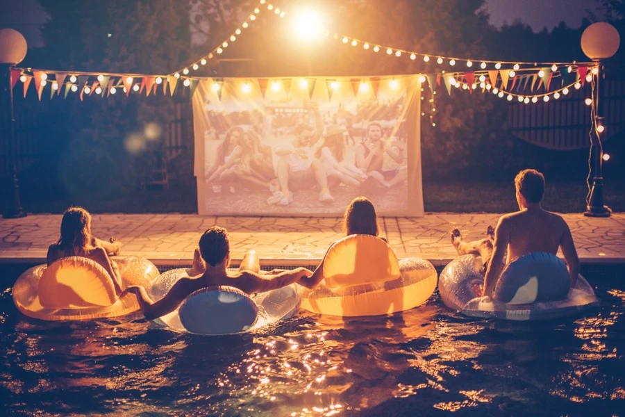 Giovani amici che hanno una festa notturna al cinema in piscina