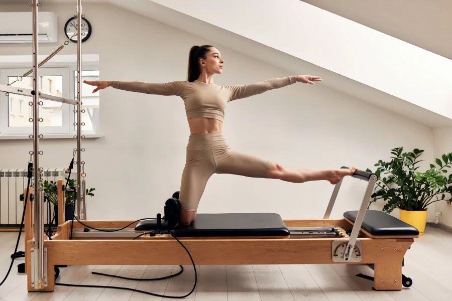 Young girl is doing Pilates on a reformer bed in a bright studio