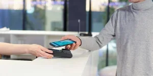 Young man in grey pullover holding smartphone with online banking page on screen
