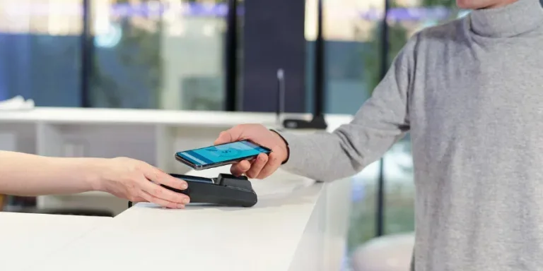Young man in grey pullover holding smartphone with online banking page on screen
