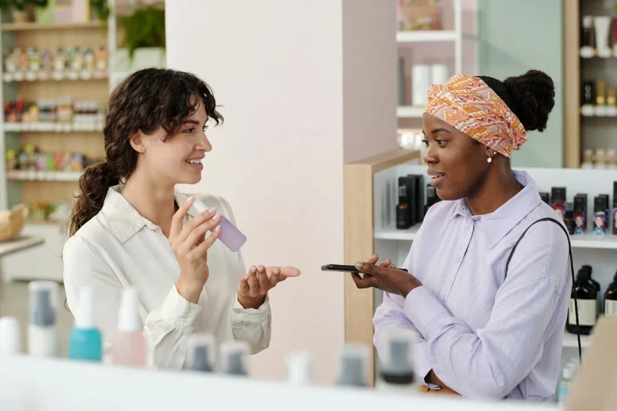 Young smiling shop assistant recommending black woman cosmetic product