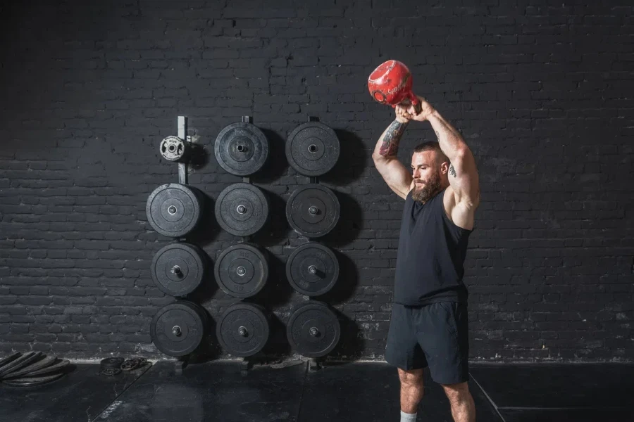 Young sweaty muscular strong fit man with big muscles doing hardcore cross kettlebell swing workout training in the gym