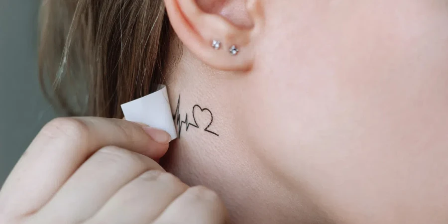 Young woman applying a temporary mini tattoo in the form of a heart and a cardiogram on her neck