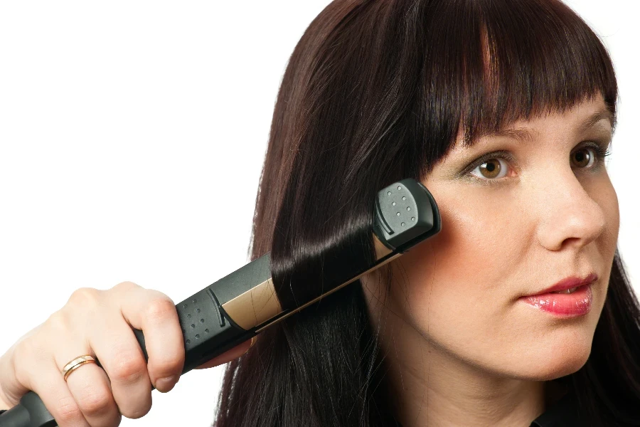 Young woman using hair straightener isolated on white