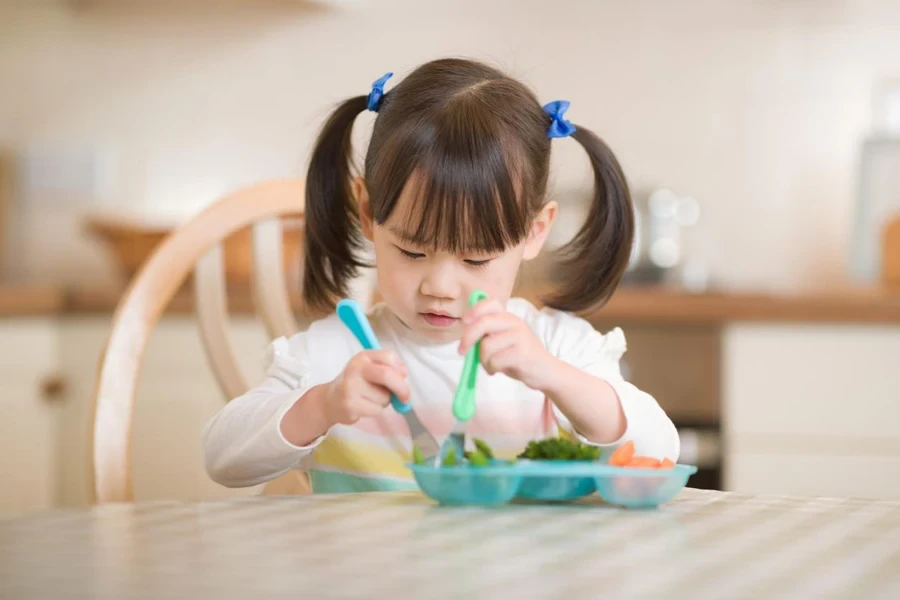 a girl is using her special designed utensil for kid to eat