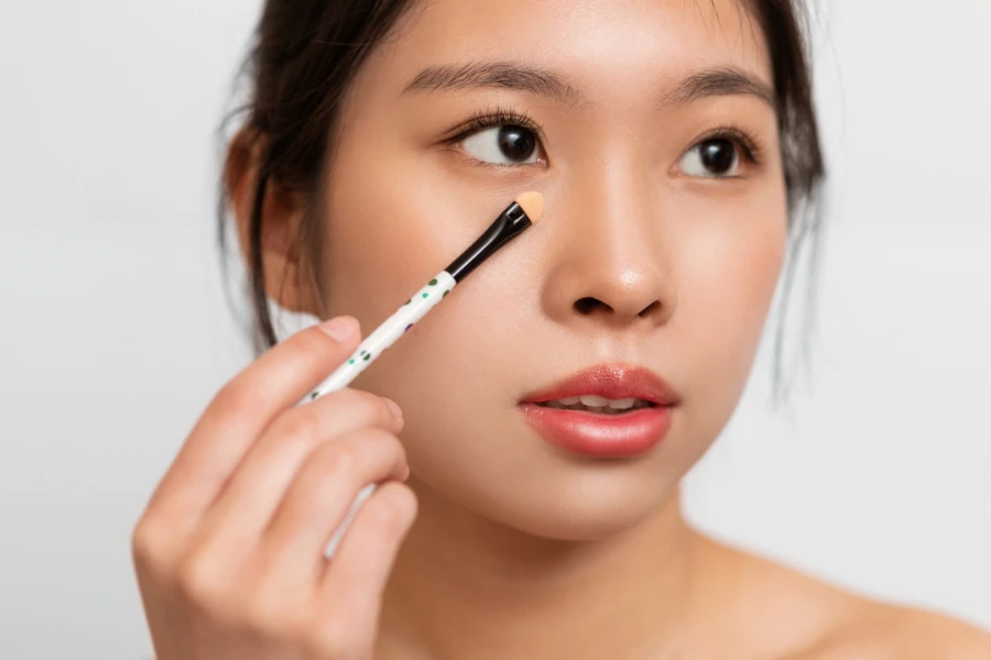 a lady using cosmetic brush to apply concealer under her eyes