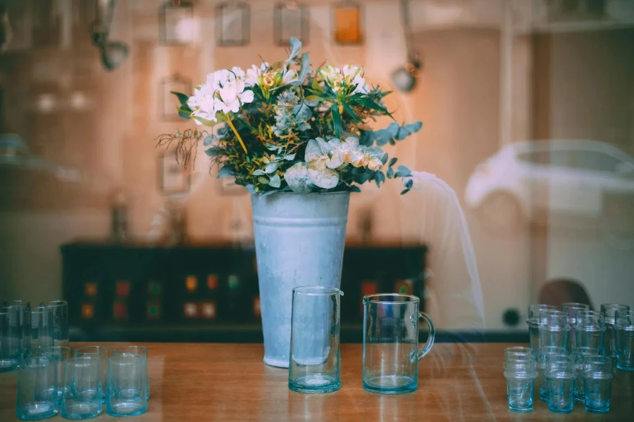 A metal flower vase beside glasses on a table