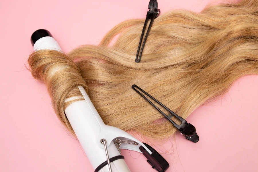 a pink background. Curl care, hair styling, black clips