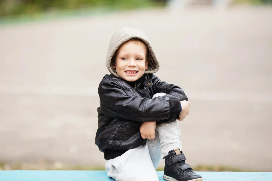 Adorable boy wearing a leather jacket and whitish gray sweatpants