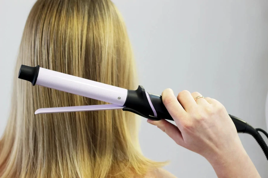 hand holds a hair curler on the background of the natural hair of a woman golden blond