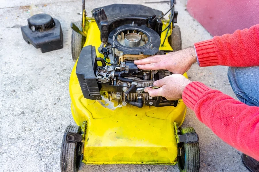 hand of man repairing old grass cutter with tools on cement floor