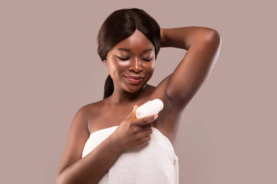 Portrait of smiling black woman applying roller deodorant