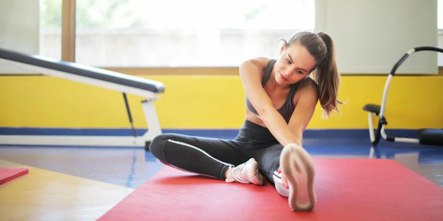 Woman in Black Sports Bra and Black Legging Sitting on Red Yoga Mat