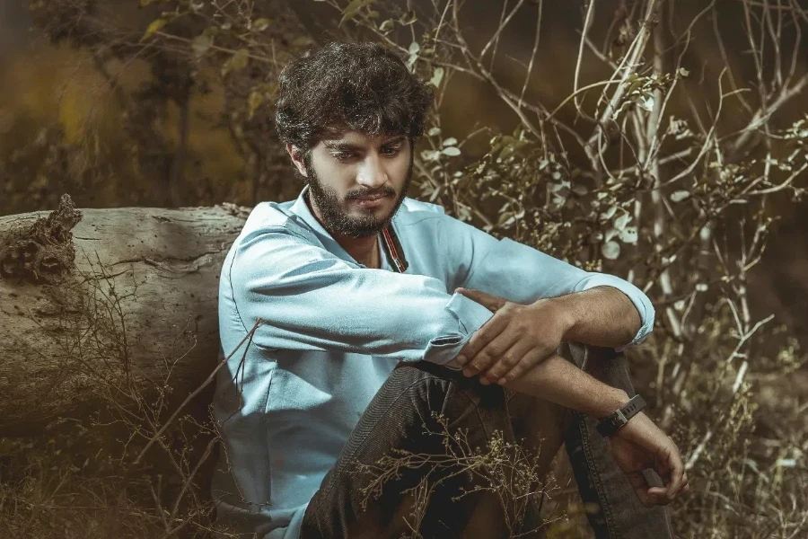 Man Sits on Grass While Leaning on Wood