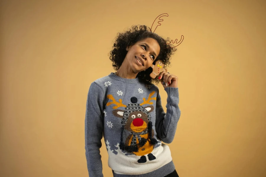 a Woman in a Sweater Holding a Gingerbread Man Cookie