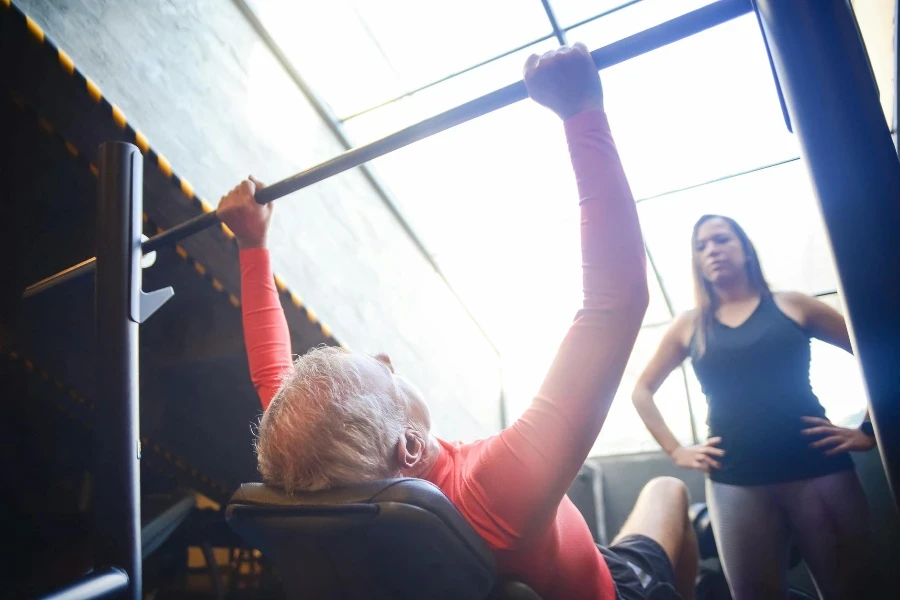 Woman in Black Tank Top Looking at a Man Lifting a Bar