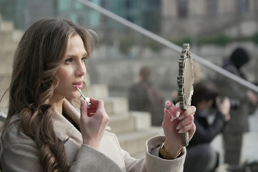 A woman is looking at her phone while holding a mirror