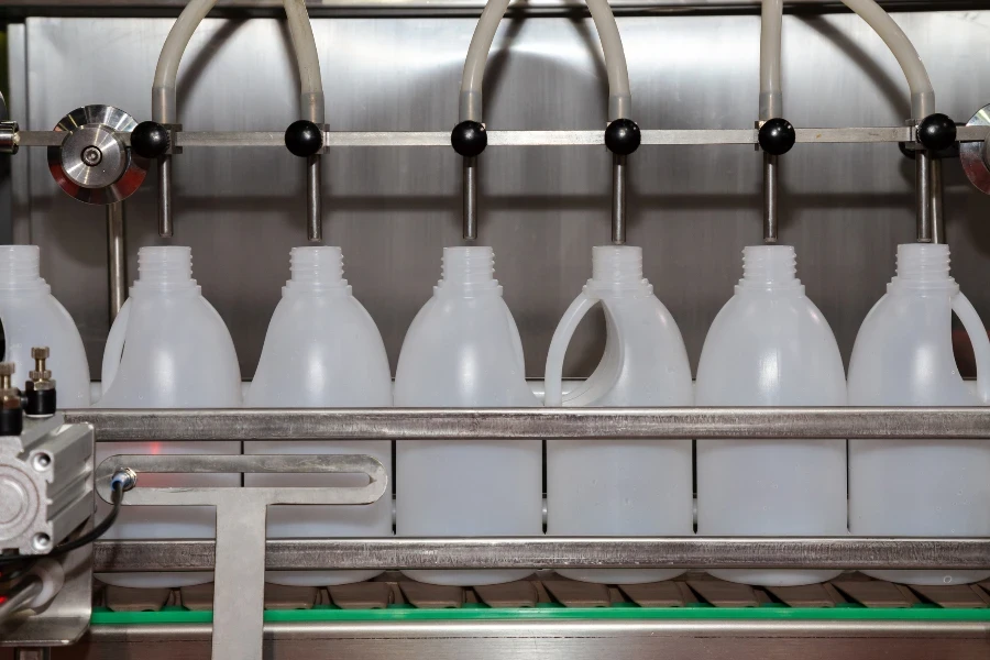 white plastic gallons or bottles on the production line of the conveyor at filling machine in the factory