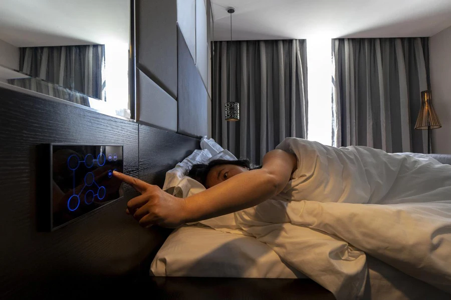 woman sleeping on bed, pushing button to open curtain, in a smart hotel