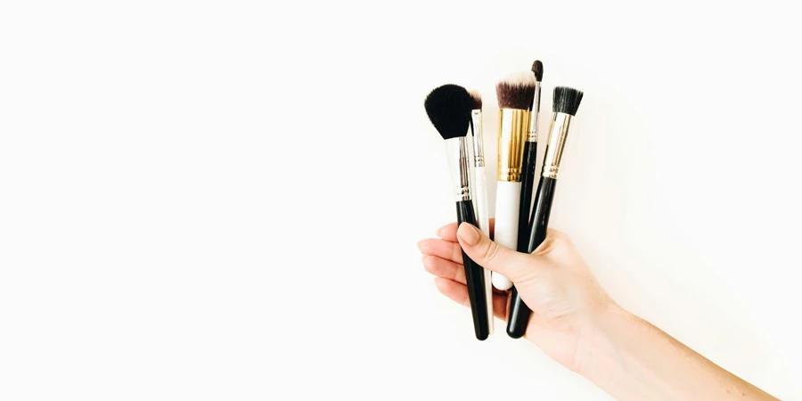 A Hand Holding Makeup Brushes on a White Background