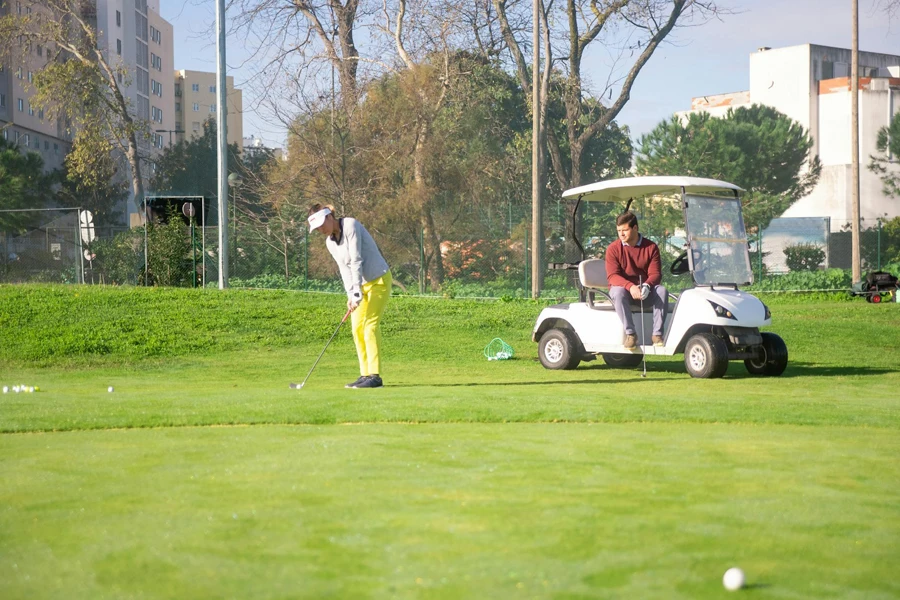 A Man Sitting on Golf Cart while Looking at the Woman in Yellow Pants Playing Golf