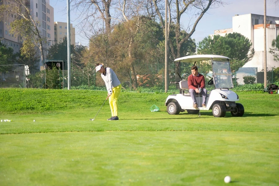 A Man Sitting on Golf Cart while Looking at the Woman in Yellow Pants Playing Golf