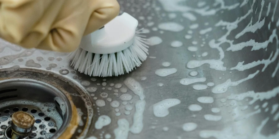 A Person in Yellow Rubber Gloves Cleaning Stainless Sink by Liliana Drew