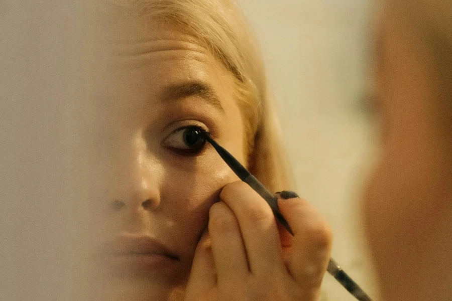 A Woman Looking at the Mirror while Applying Eyeliner